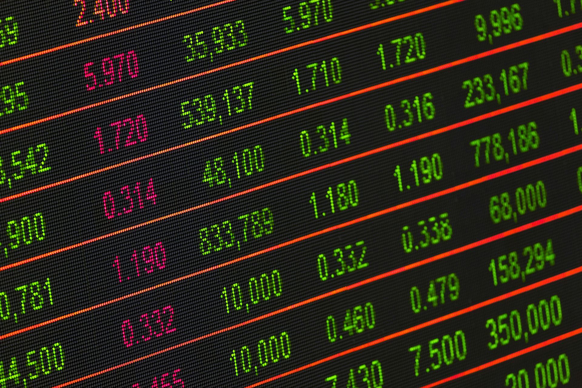 A close-up of a digital stock market display screen featuring columns of green and red financial data and numbers.
