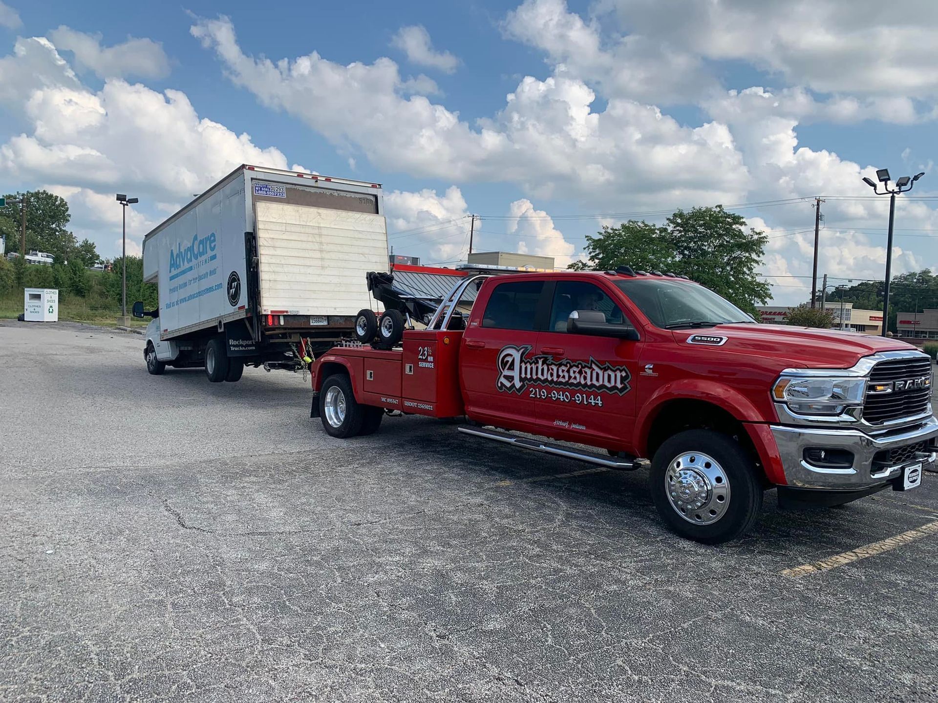 Red tow truck towing a trailer with a white box on a sunny day.