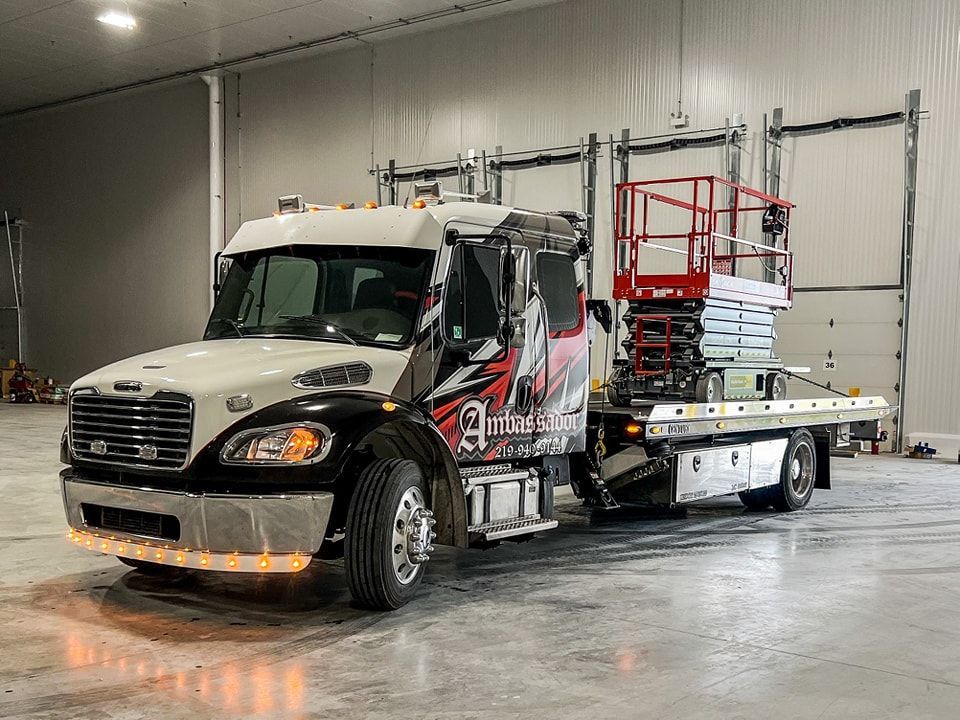 White and black work truck with aerial lift on flatbed, parked inside a warehouse.