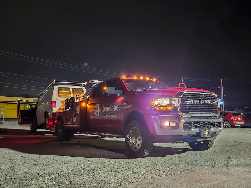 Tow truck with a white van at night. The truck is red with its lights on.