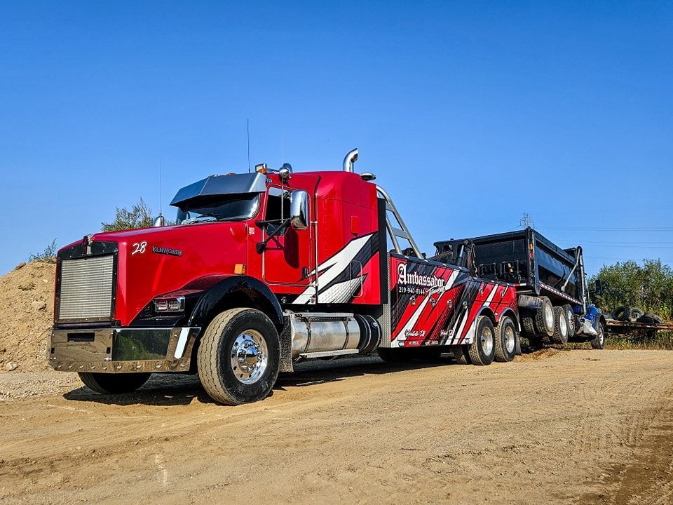 Red tow truck with black trailer on dirt road under a clear blue sky.