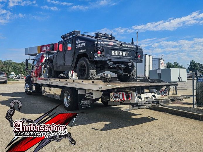 Black armored Sheriff's vehicle on a flatbed tow truck; parked outdoors under a bright blue sky.