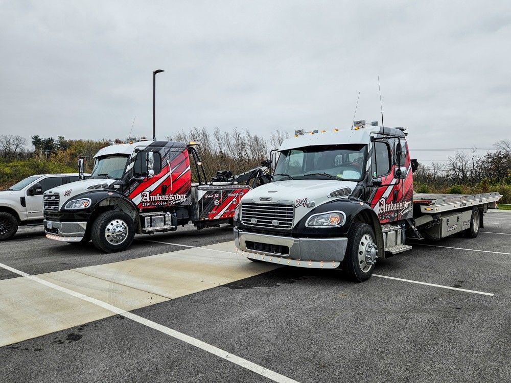 Two tow trucks parked on pavement, under an overcast sky.