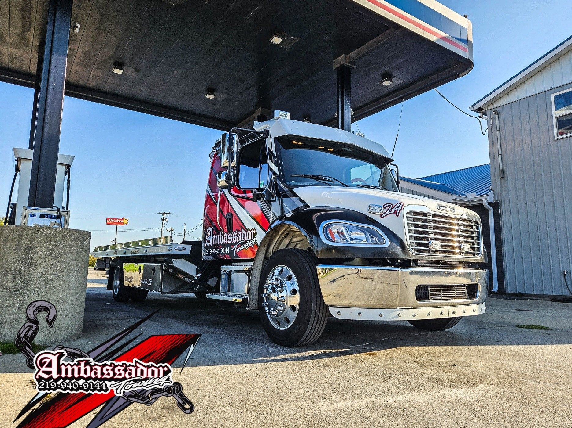 A flatbed truck with a custom design is parked under a gas station canopy.