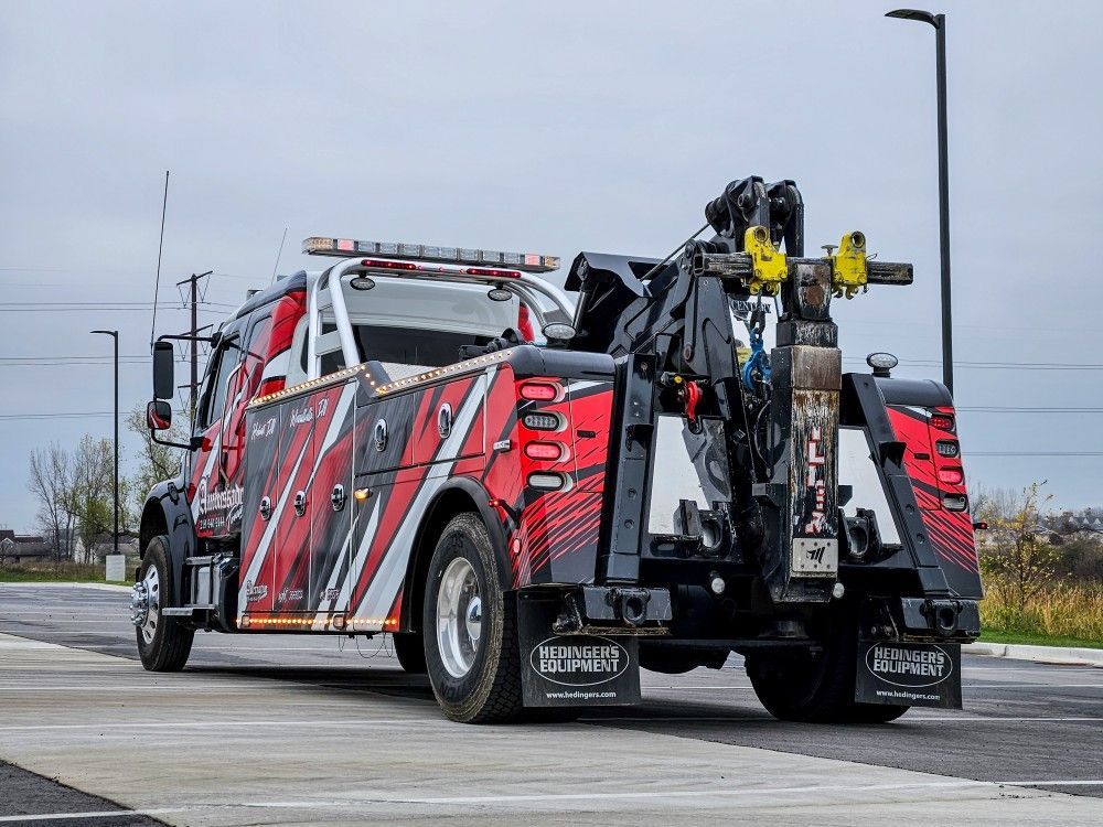Tow truck, red and black design, rear view, tow boom extended, on asphalt.