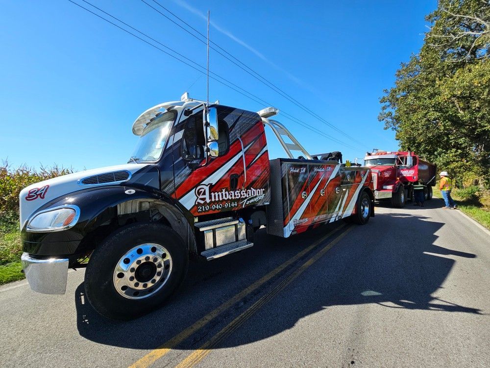 A tow truck with red and black graphics towing a red vehicle on a sunny roadside.
