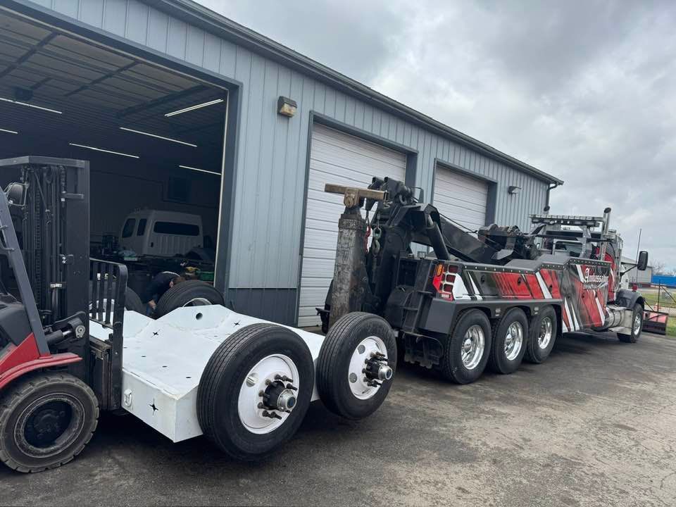 A forklift and a tow truck parked in front of a gray garage.