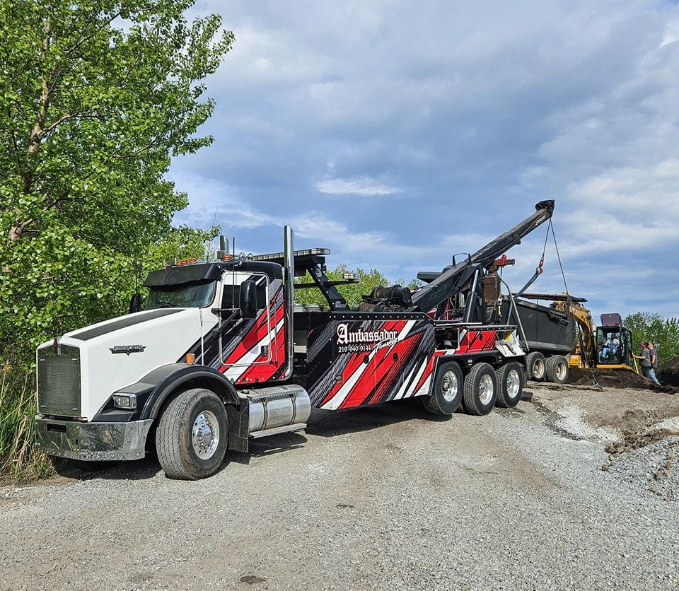 Tow truck at a construction site; white and red truck with arm extending to a dump truck and excavator.