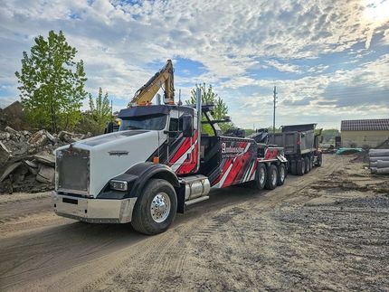 White and red tow truck with excavator loading a dump truck at a construction site.