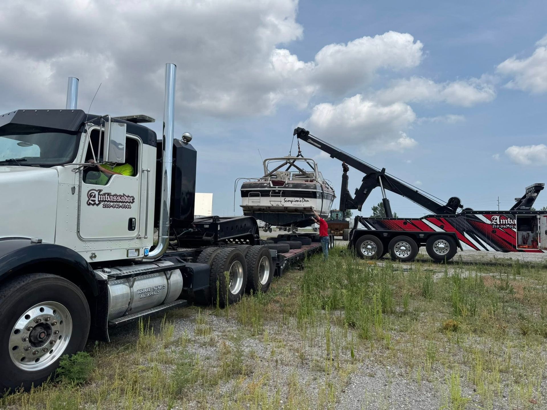 Tow truck loading a boat onto a semi-truck. The scene is outdoors with a cloudy sky.