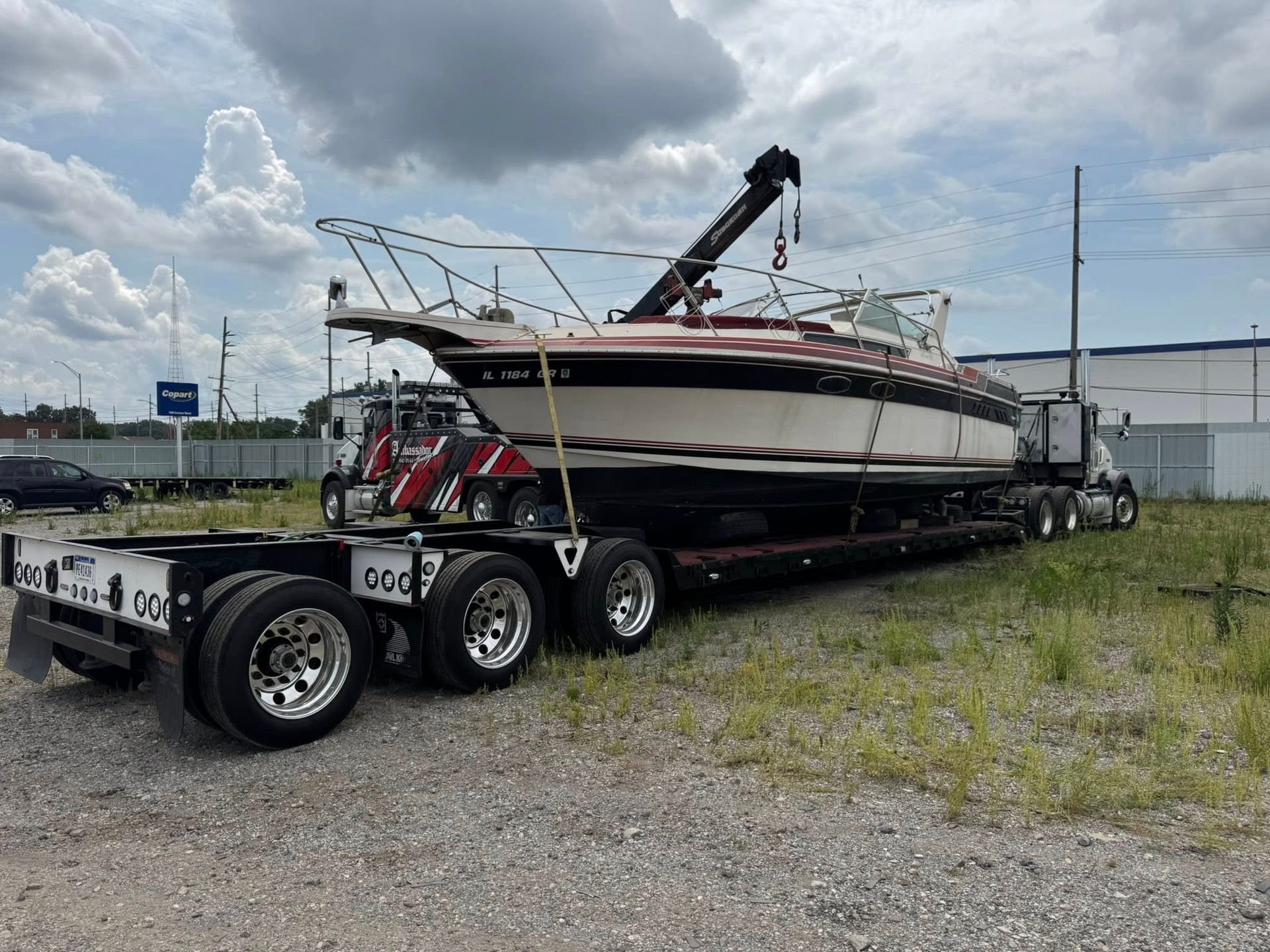 Boat being transported on a flatbed truck; crane extended, blue sky background.