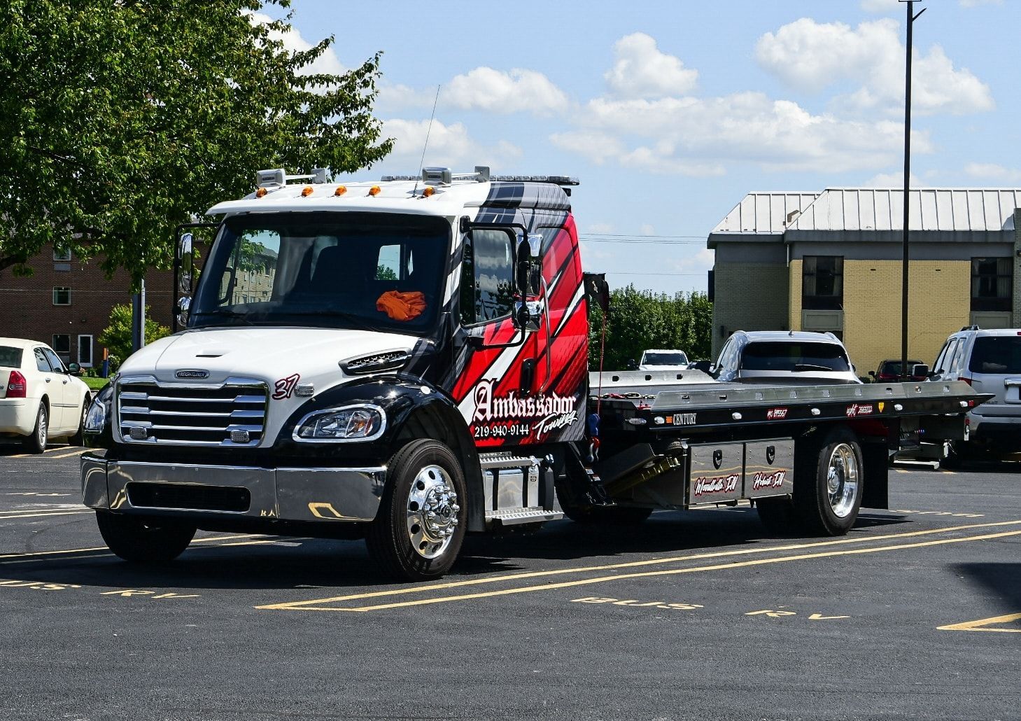 Tow truck, black and red, parked in parking lot. Silver car on the back.