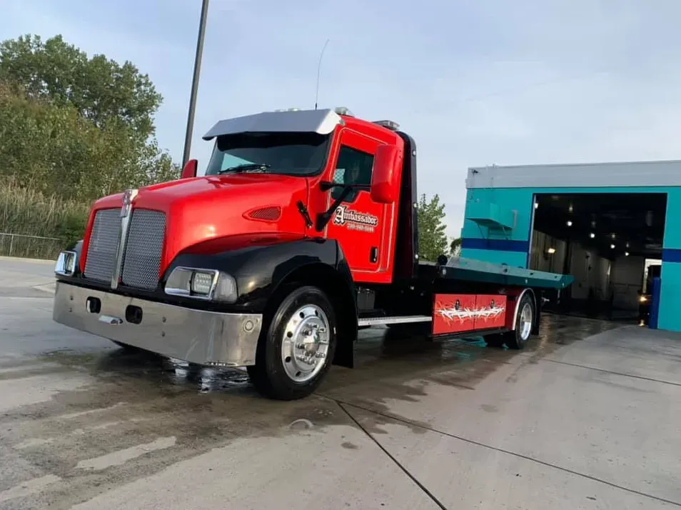 Red and black tow truck with silver details parked in front of a blue garage.