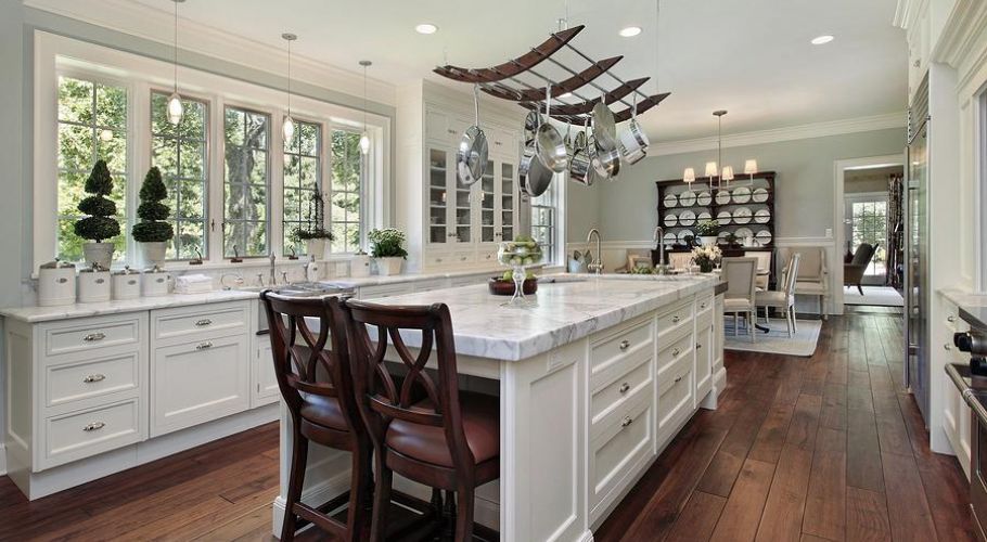 A kitchen with white cabinets , a large island , and hardwood floors.