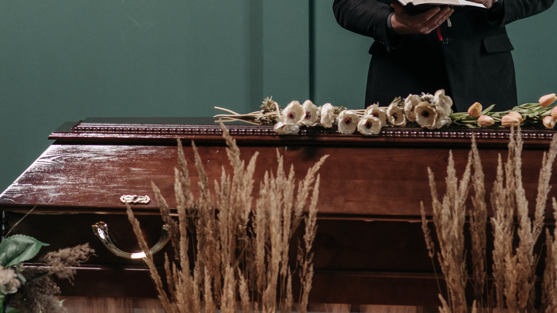 A man is standing in front of a coffin with flowers on it.