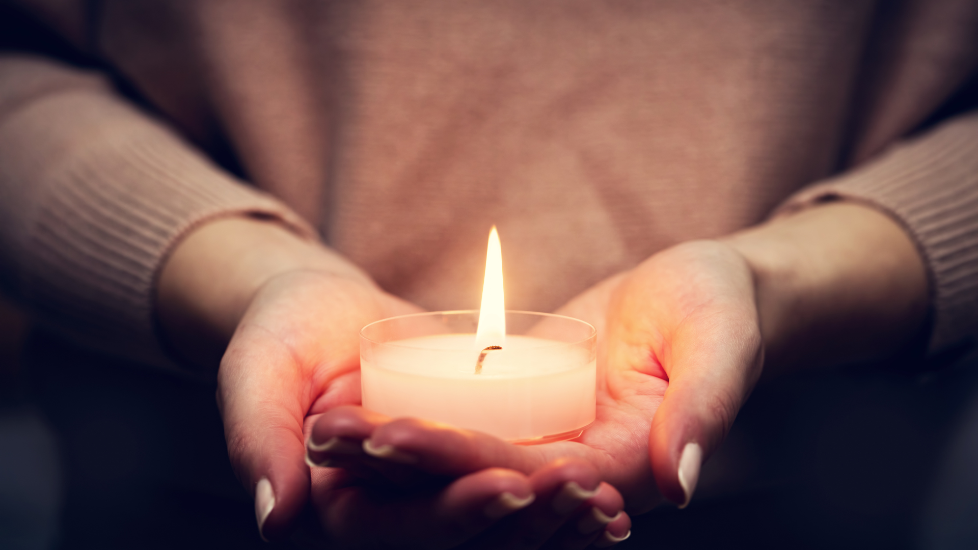 A woman is holding a lit candle in her hands.