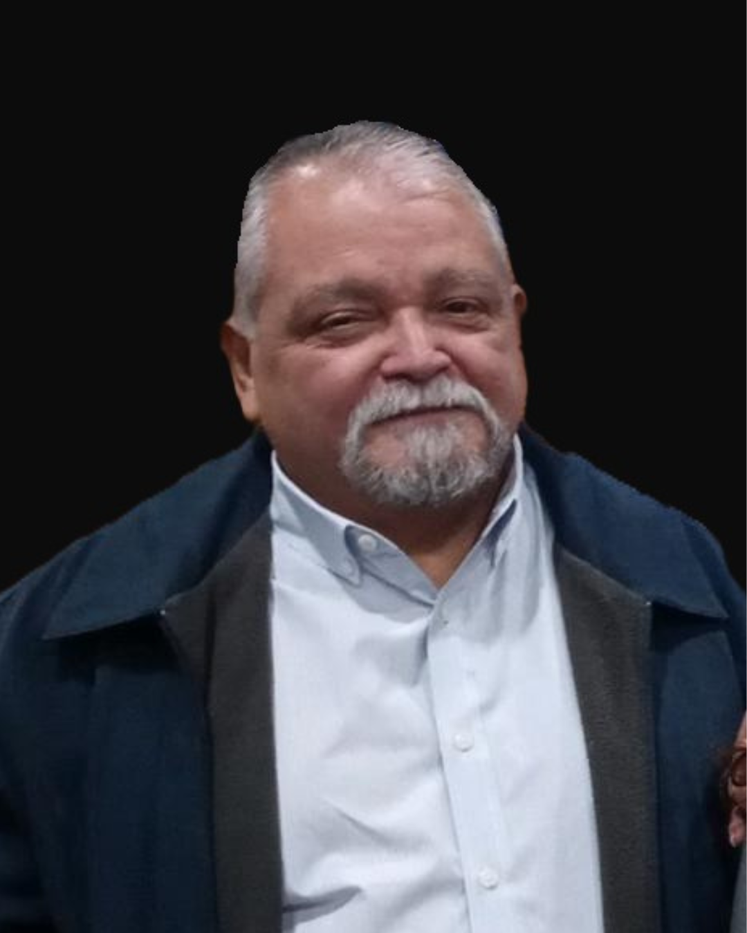 Man in light blue shirt and dark jacket smiles at the camera, with a graying goatee.