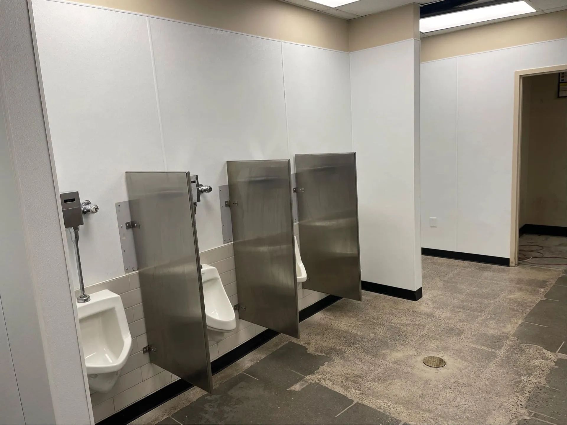 A public restroom with urinals and stainless steel dividers.