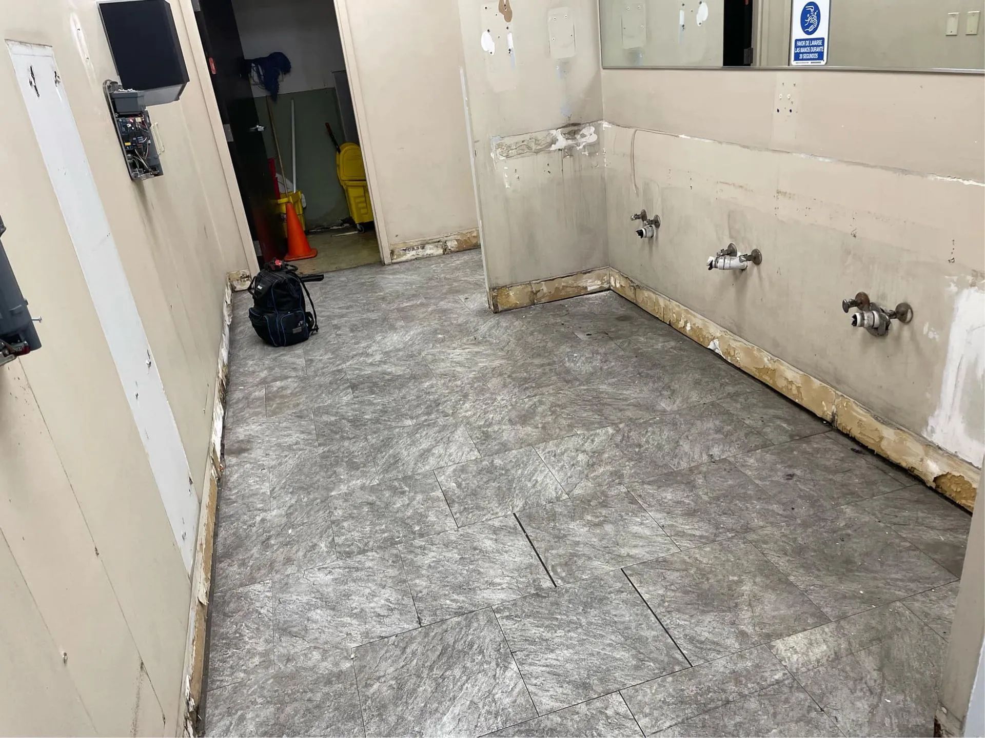 A bathroom with a dirty floor and a mirror.