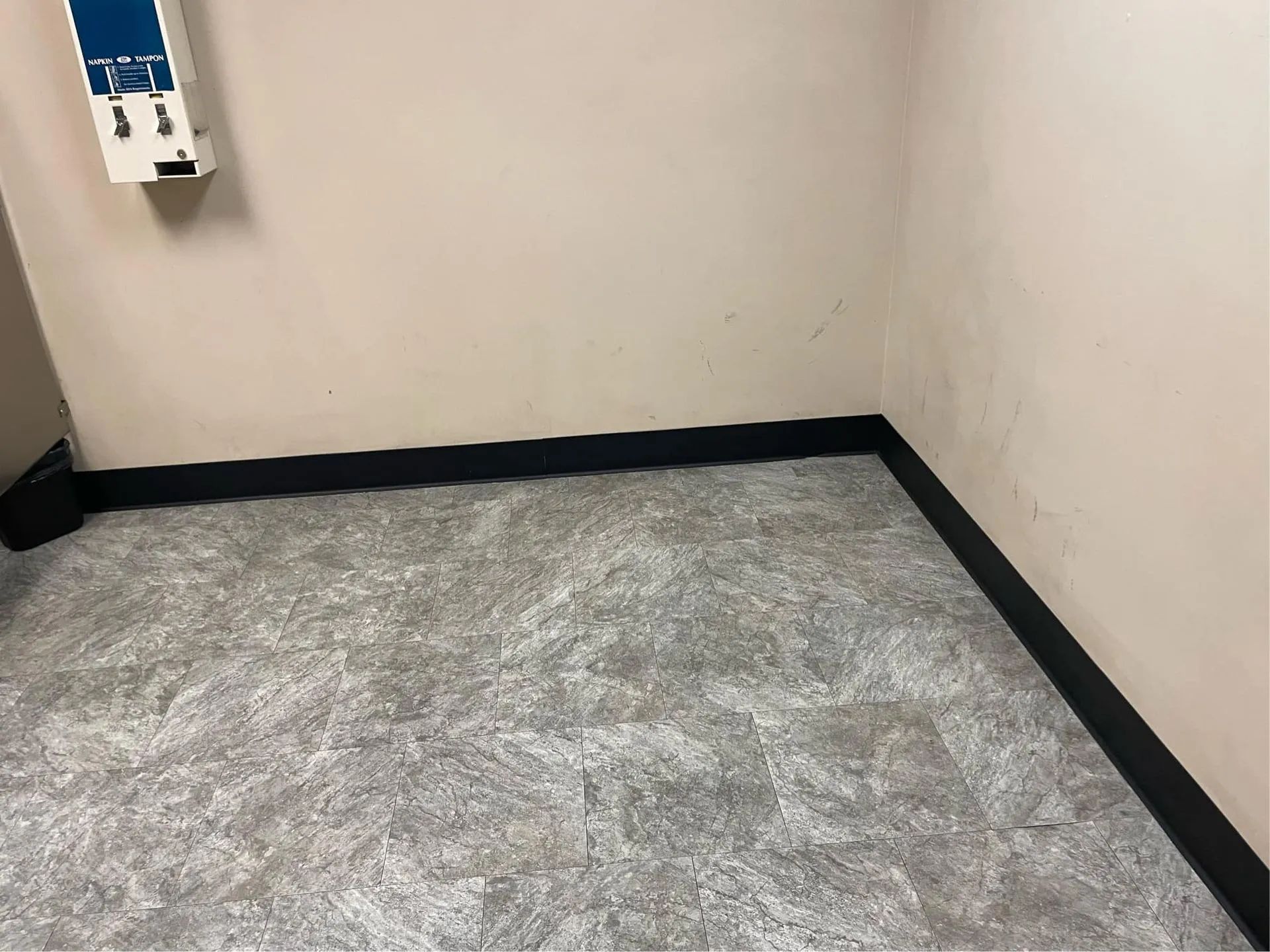A corner of a room with a gray floor and a white wall.
