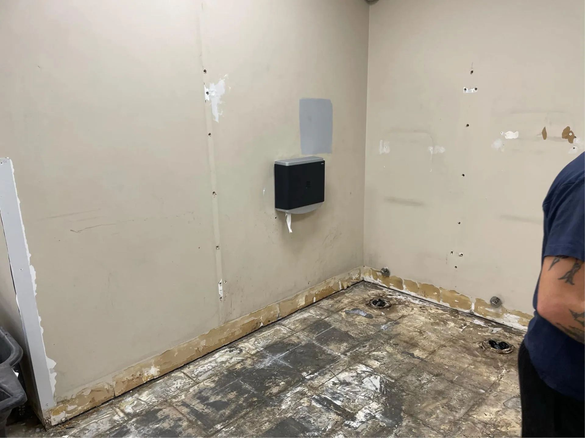 A man is standing in a room with a toilet paper dispenser on the wall.