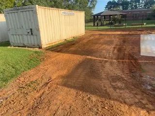 A shipping container is sitting in the middle of a dirt road.