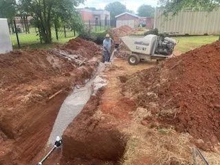 A man is standing in a pile of dirt next to a dump truck.