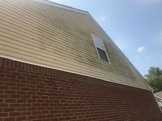 A brick house with a white siding and a window on the side.