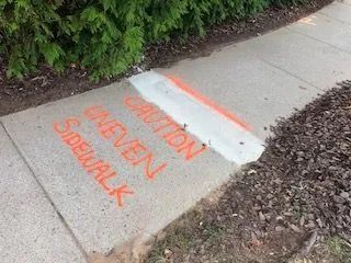 A sidewalk with the words `` caution one even sidewalk '' spray painted on it.
