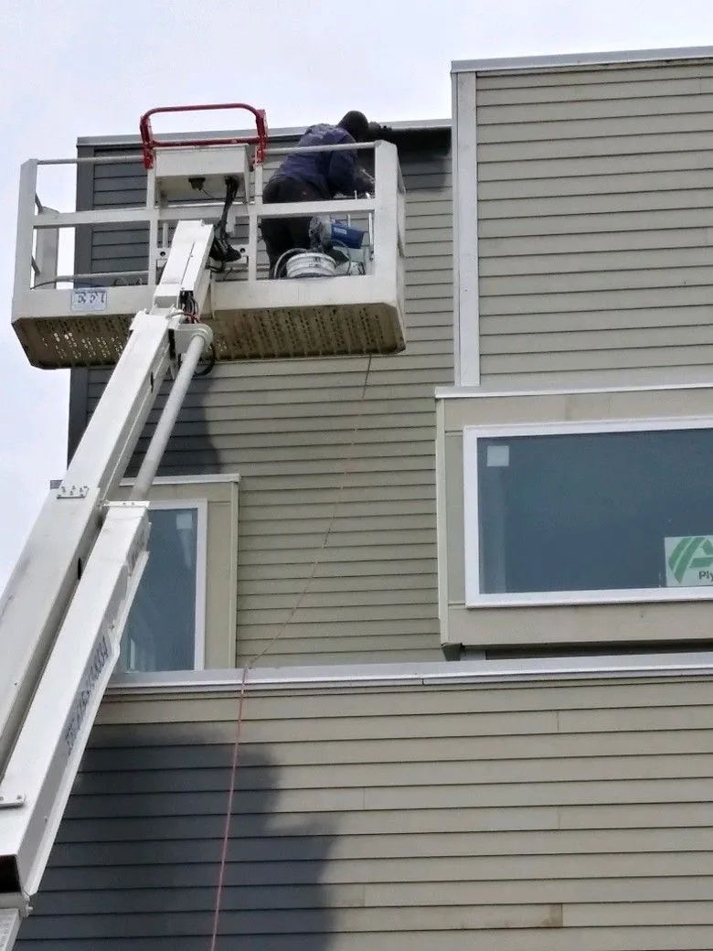 A man is standing in a bucket on top of a building.