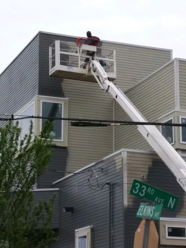 A man on a crane is painting the side of a building