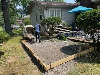 A man is loading concrete into a wheelbarrow in front of a house.