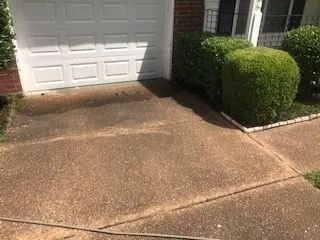 A driveway with a garage door and bushes in front of it.