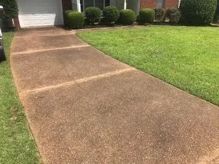 A concrete walkway leading to a house with a lush green lawn.