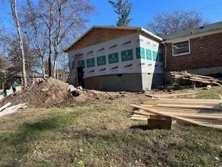 A house is being remodeled and a large pile of wood is in front of it.