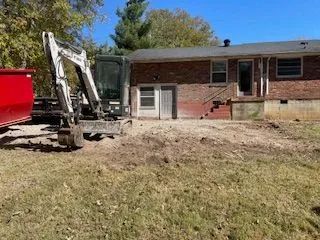 An excavator is sitting in front of a brick house.