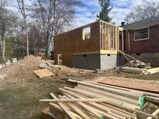 A house under construction with a pile of wood in front of it.