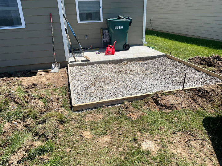 A concrete patio is being built in the backyard of a house.