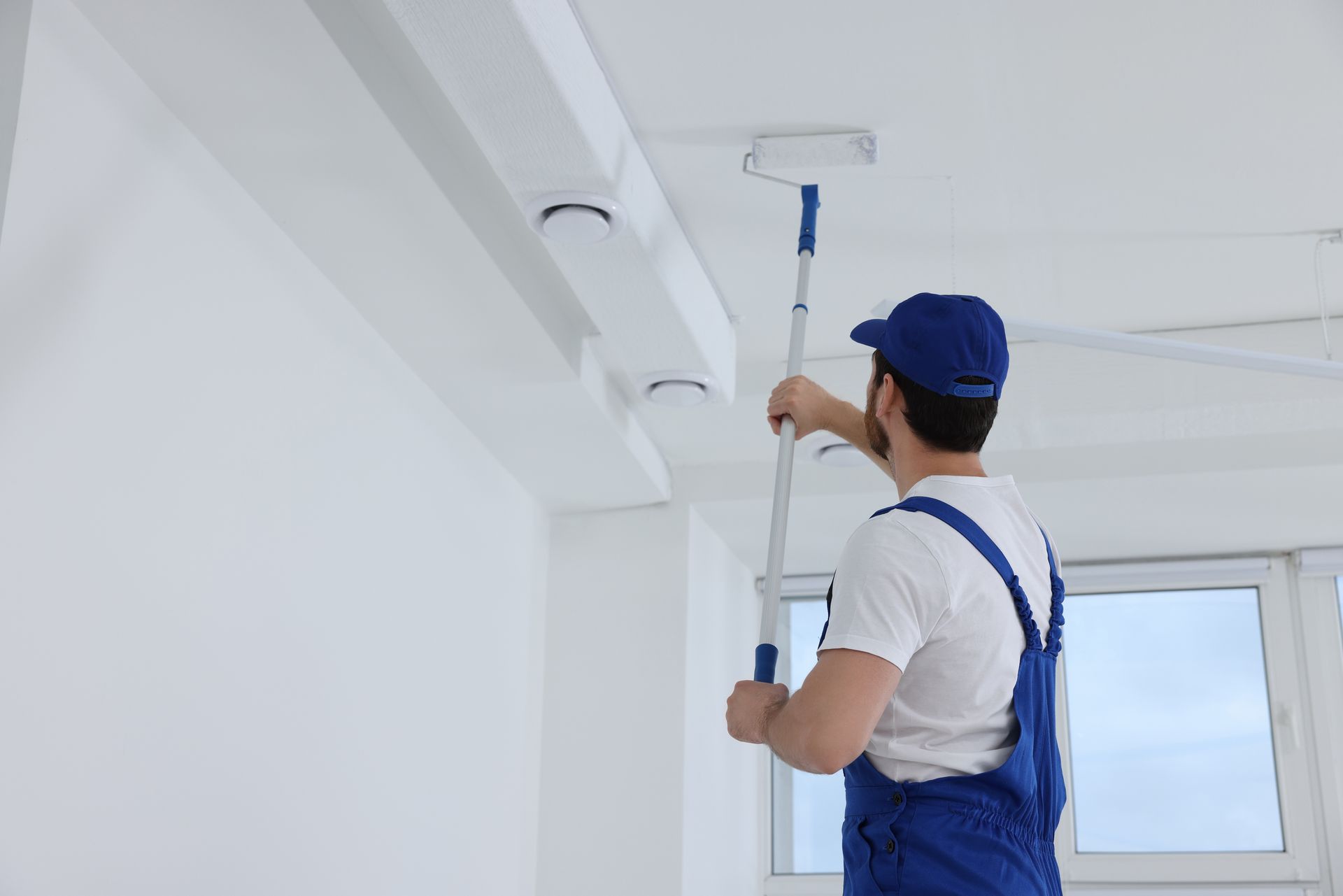 A man is painting the ceiling of a room with a roller.