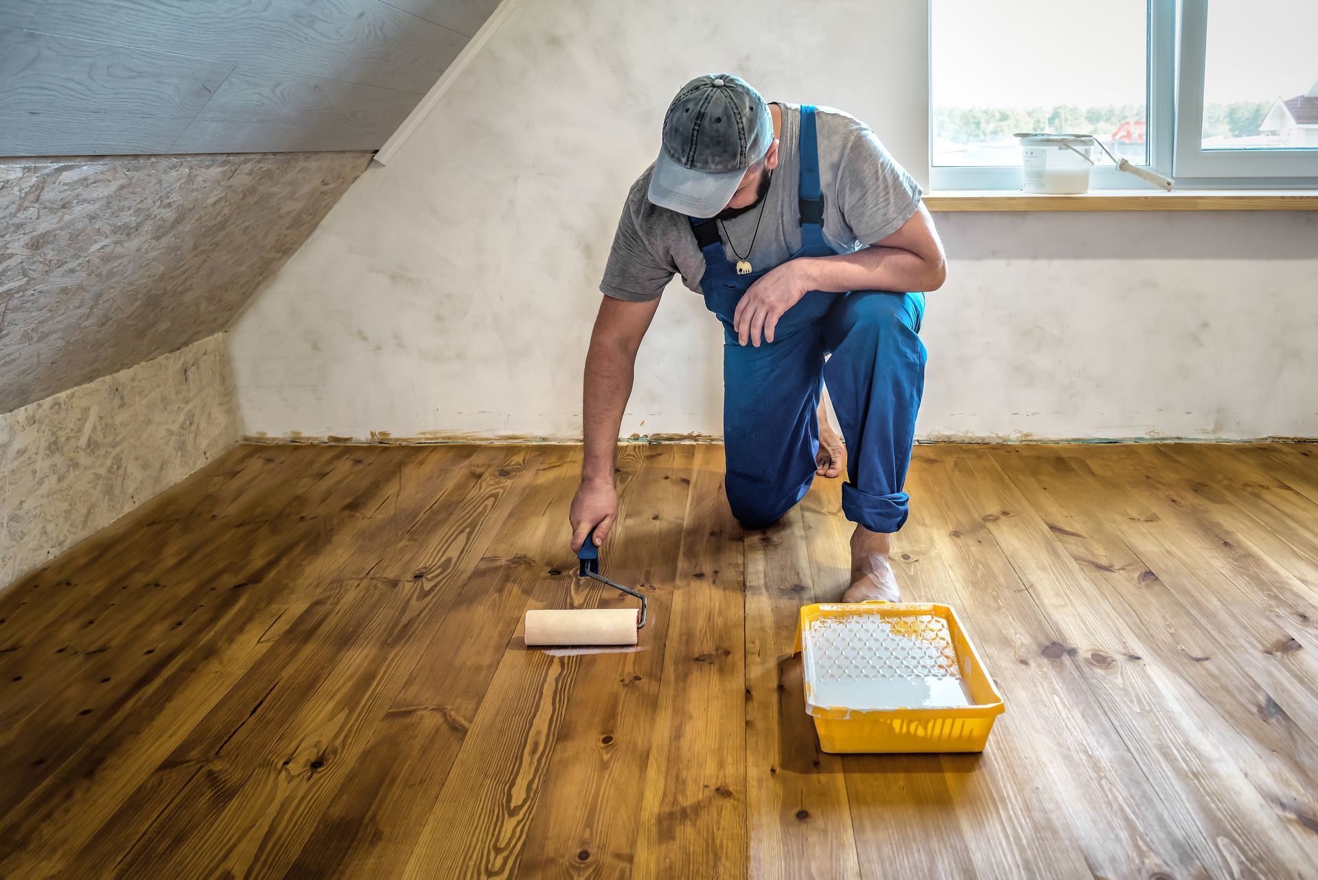 A man is painting a wooden floor with a roller.