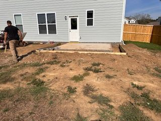 A man is standing in the dirt in front of a house.