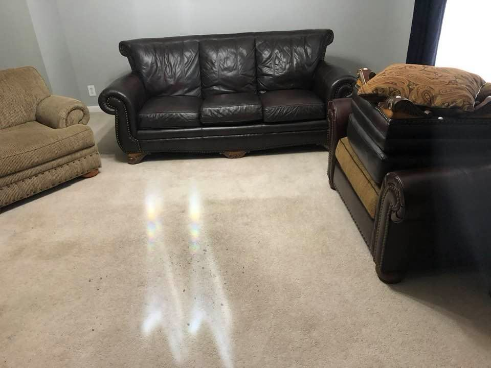A living room with a couch and two chairs and a cat laying on the couch.