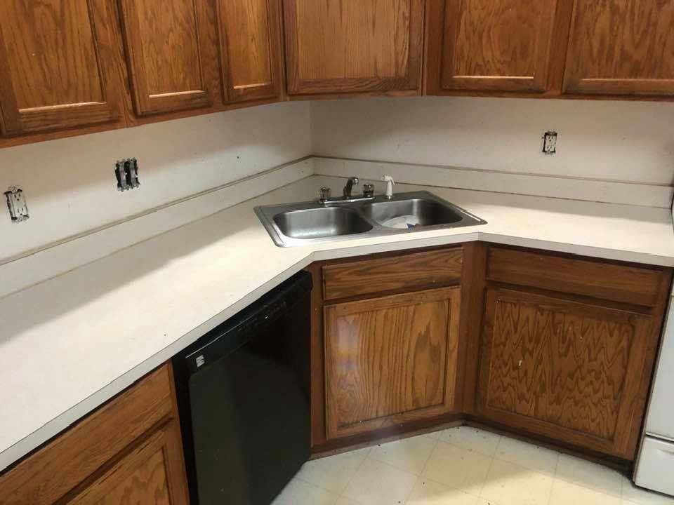 A kitchen with wooden cabinets , a sink , and a black dishwasher.