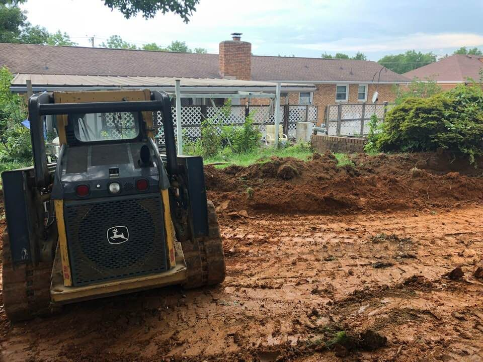 A john deere bulldozer is sitting in the dirt in front of a house.