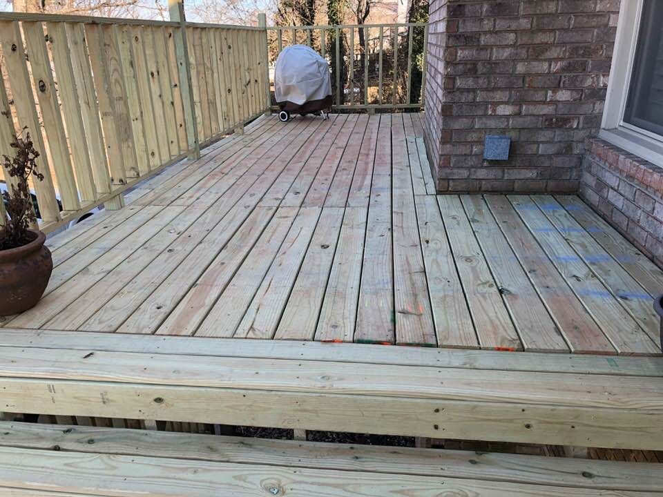 A wooden deck with a grill on it next to a brick house.