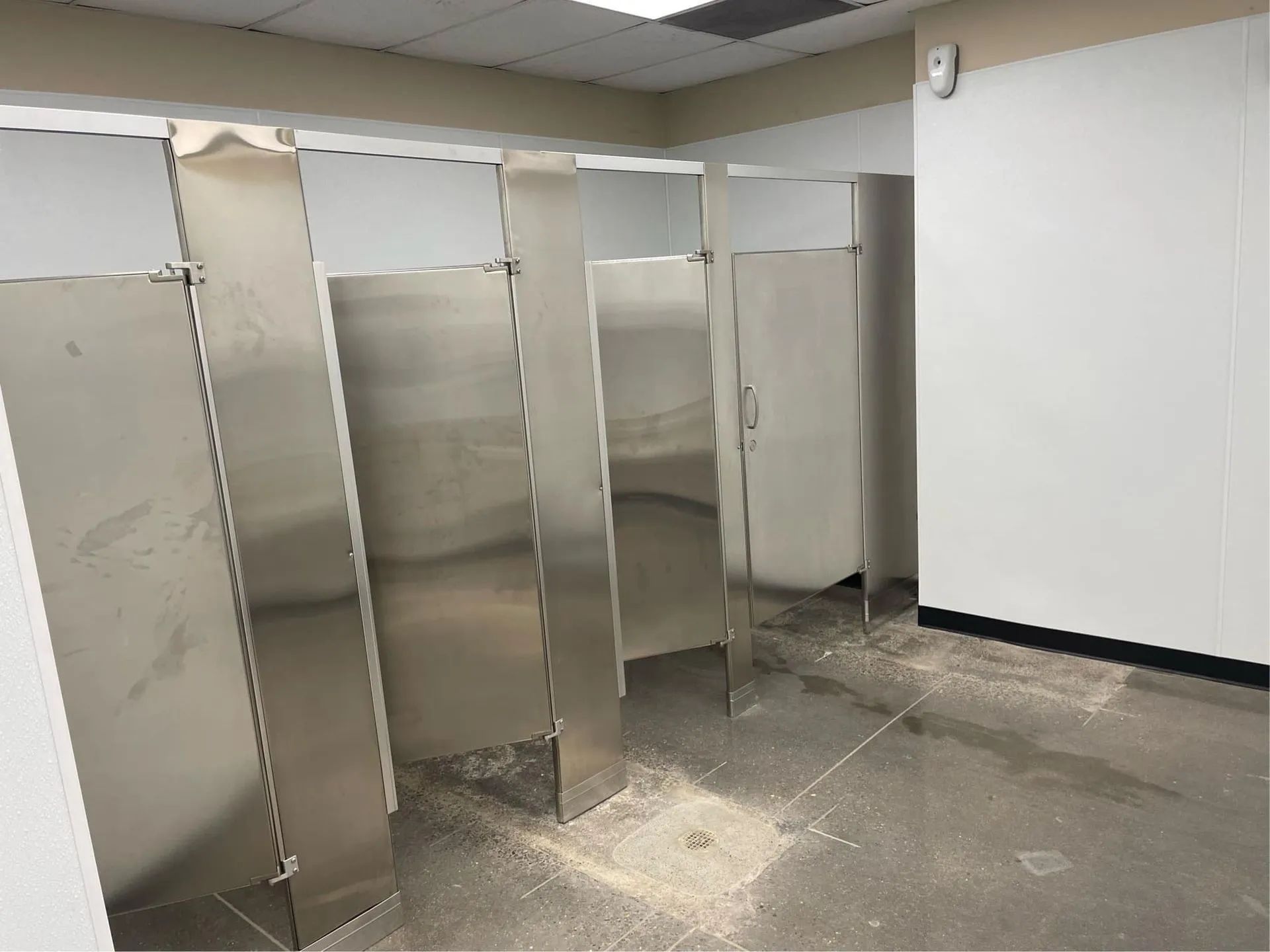 A bathroom with stainless steel stalls and white walls