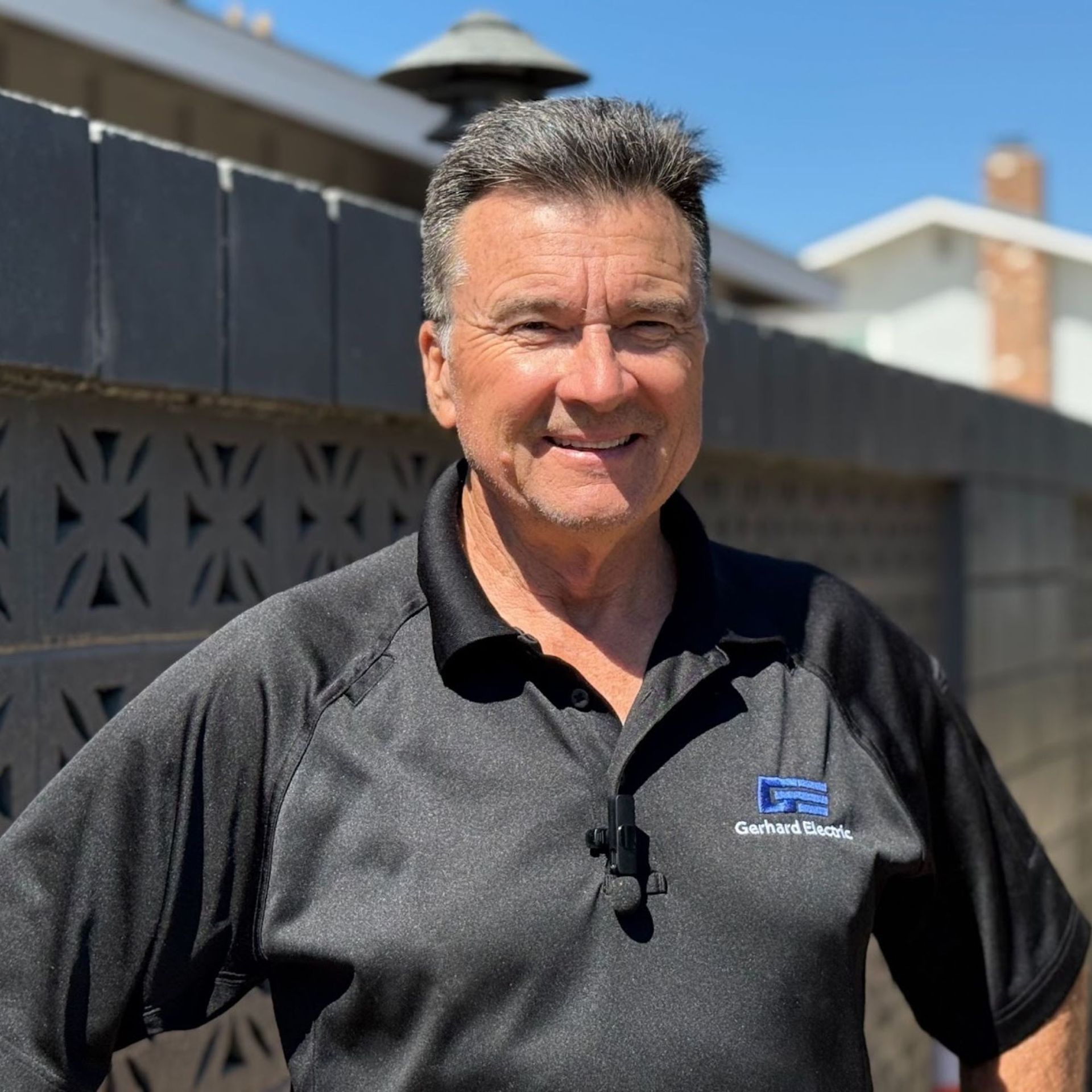 Man in black polo smiling, standing outside in front of a decorated fence.