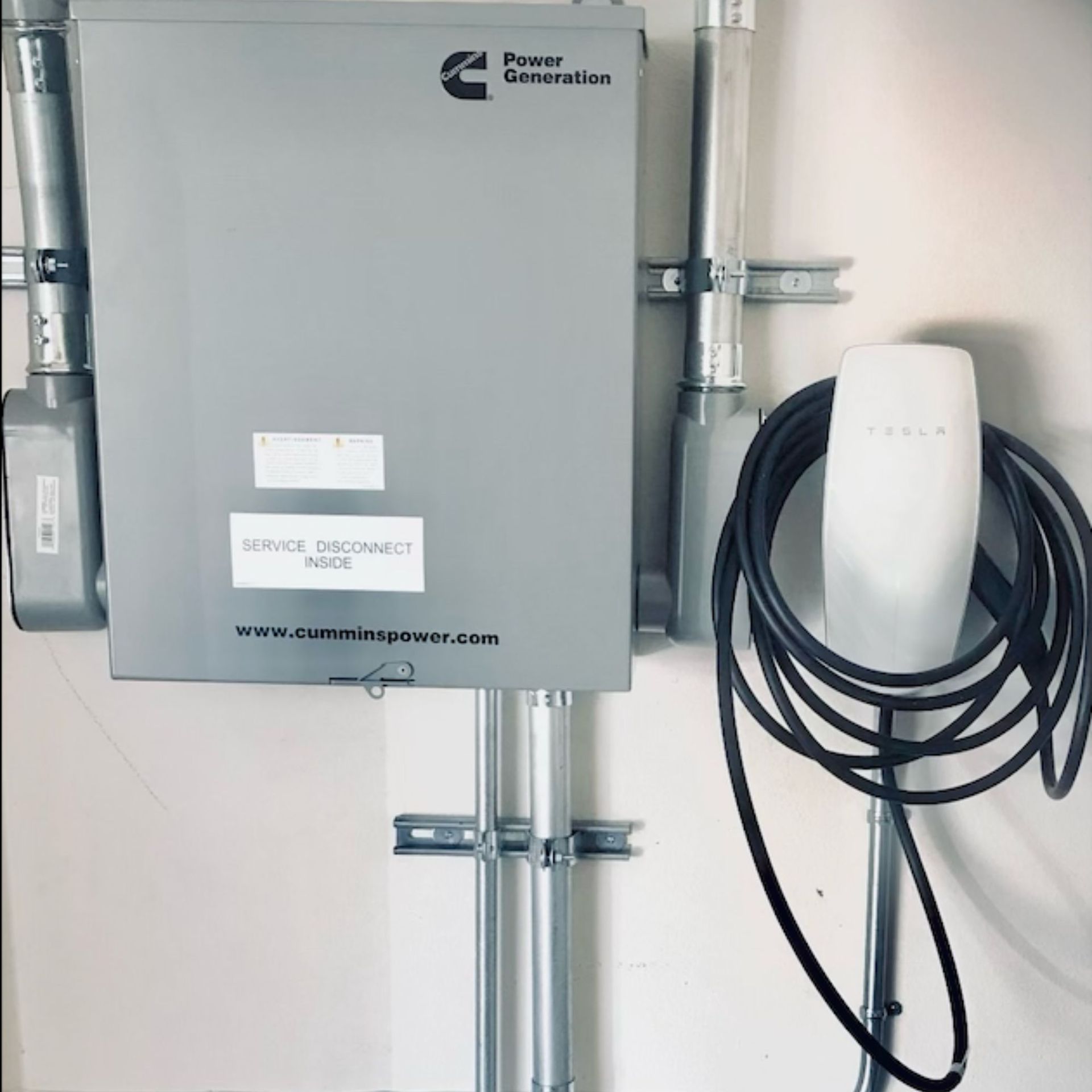 Grey electrical box and Tesla charger mounted on a white wall.