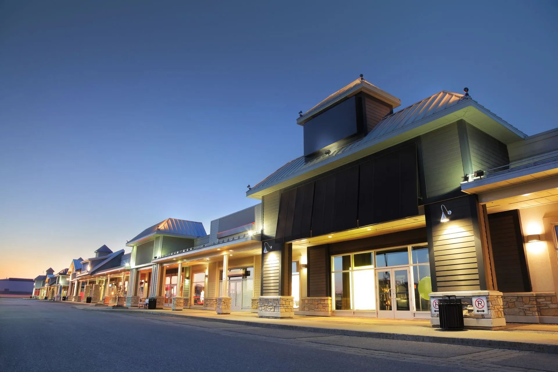 A row of stores are lit up at night in a shopping center.
