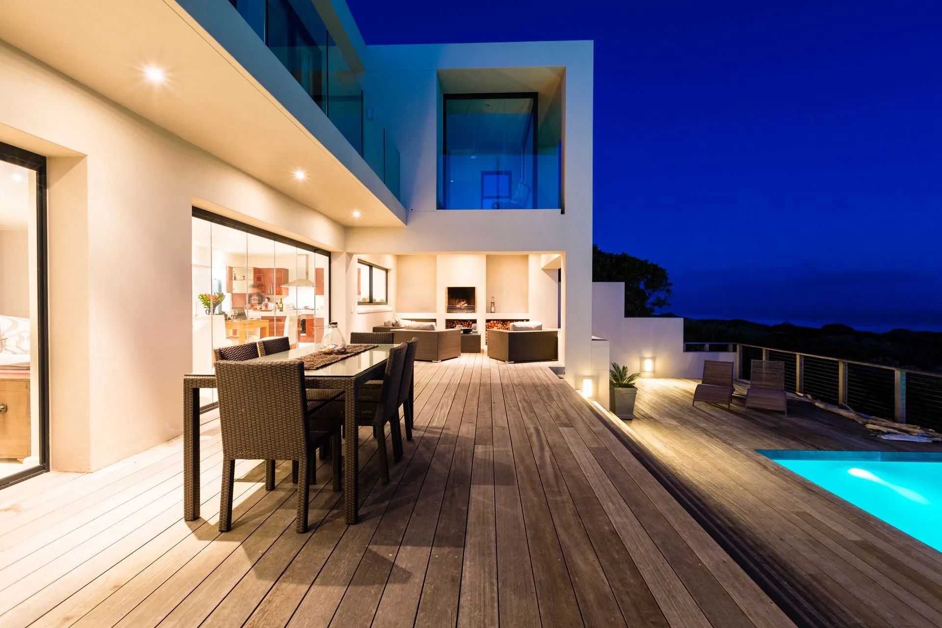 A large house with a swimming pool and a wooden deck at night.
